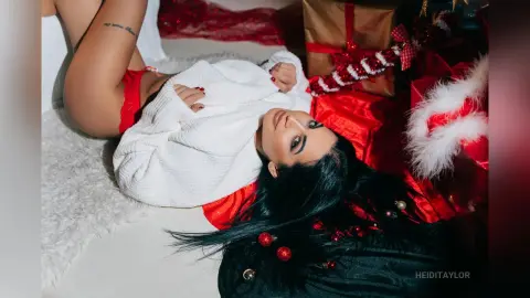 Woman in white sweater lying on white faux fur near red Christmas gifts in a festive holiday mood.