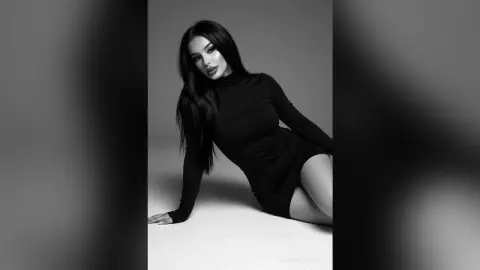 Elegant woman in a black long-sleeve dress posing against a minimalist studio background in a moody black and white style.