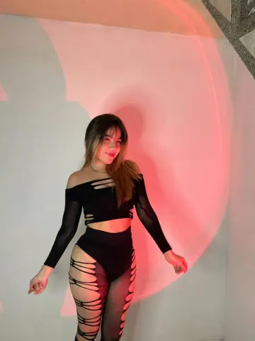 Young woman in a black cutout crop top and mesh leggings posing against a red light background.