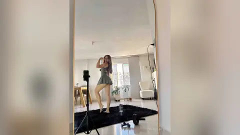 Young woman in a grey mini dress taking a mirror selfie in a bright, modern minimalist living room.