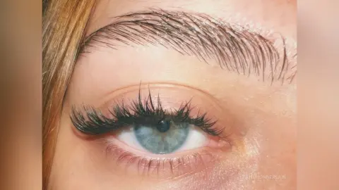 Close-up of a woman's blue eye featuring long voluminous eyelash extensions and groomed eyebrows.