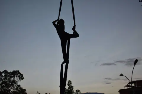 Silhouette of an aerialist performing on a single trapeze swing against a twilight sky at dusk.