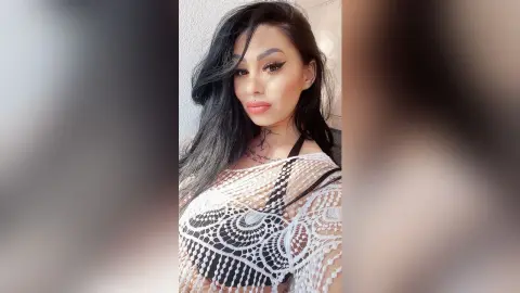 DeeaAnderson poses with long black hair wearing a white lace mesh top.