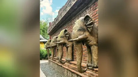 Large stone elephant statues standing against a rustic brick wall in a peaceful outdoor garden setting.