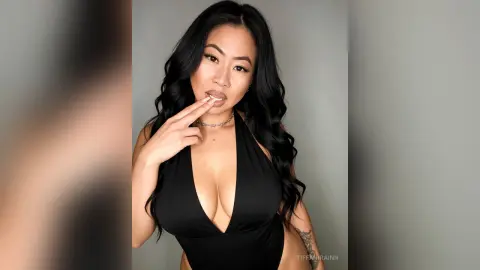 Glamorous woman with long wavy hair wearing a black plunging halter bodysuit in a studio setting.