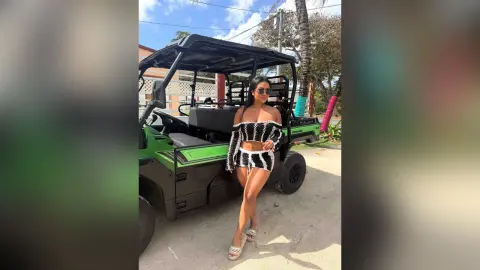 Miah stands next to a green golf cart wearing a black and white striped crop top and matching mini skirt.