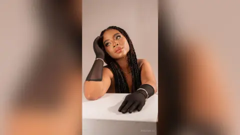 Elegant woman in black sheer gloves and gold jewelry posing against a neutral studio background.