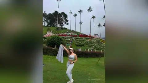 Young woman in grey yoga outfit stretching in a lush green tropical garden under palm trees.
