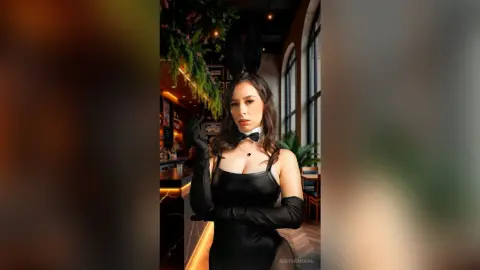 Elegant woman in black bunny costume and long gloves posing in a moody, dimly lit cocktail bar.