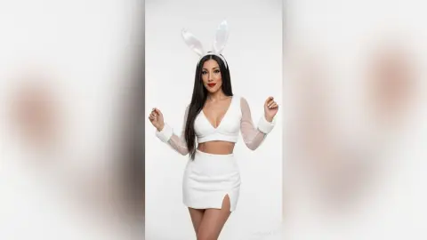 Woman in white bunny ears and crop top outfit posing against a white background for a playful photoshoot.