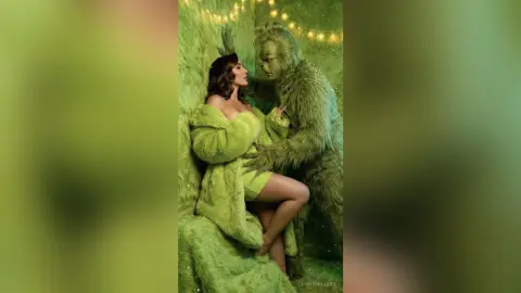 Glamorous woman in a green faux fur coat embracing the Grinch in a festive, whimsical holiday setting.