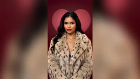 Elegant woman in a luxurious leopard print faux fur coat posing against a romantic red heart background.