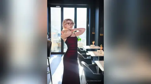 Elegant blonde woman in a sleek burgundy evening dress posing in a bright, modern minimalist dining room.