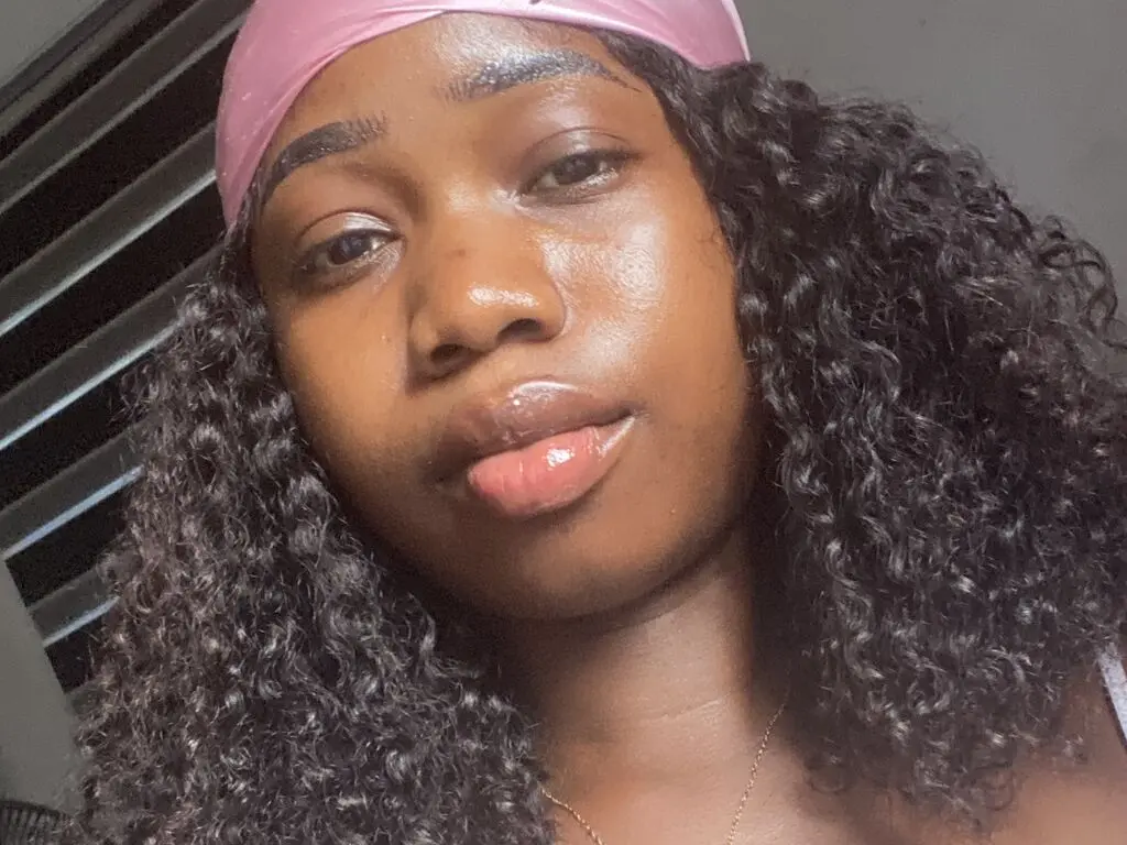 Young woman with curly hair and pink headband posing with a glowing complexion in soft natural light.