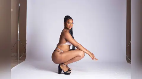 IvyBerry squats in a light pink bikini, showing her bare buttocks and back against a plain white studio background.