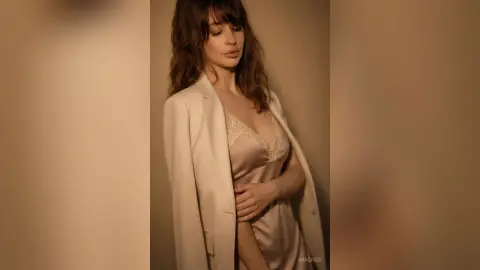 Elegant woman in a cream satin slip dress and white blazer posing in a warm, minimalist indoor setting.