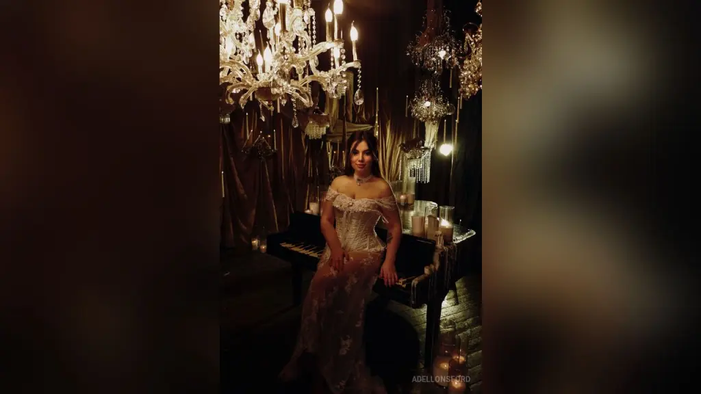AdelLonsford — AdelLonsford sits on a piano in a white lace dress under glowing chandeliers.