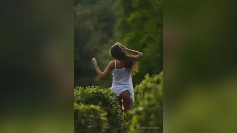 Dreamy portrait of a woman in a white summer dress running through a lush green garden at sunset.