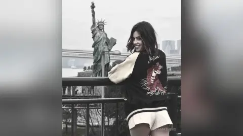 AnaMathers smiles while standing outdoors in front of the Statue of Liberty, wearing a black and white graphic sweatshirt and white shorts.