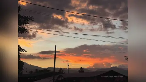 Dramatic sunset sky with orange clouds over a dark mountain landscape at dusk.
