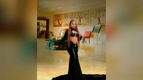 Elegant woman in a black cutout evening gown posing in a luxury hotel lobby with gold decor.