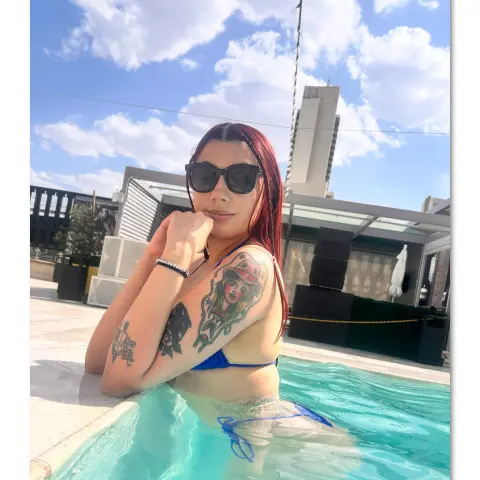 Tattooed woman in a blue bikini relaxing in a sunny outdoor swimming pool on a bright summer day.
