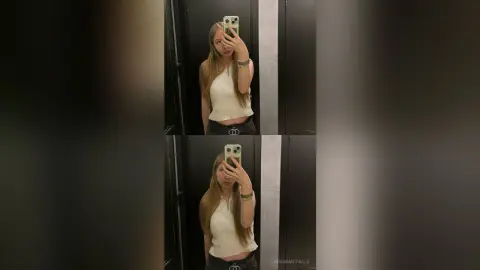 AdenaMcfalls poses for a mirror selfie wearing a white tank top and black shorts against a dark background.