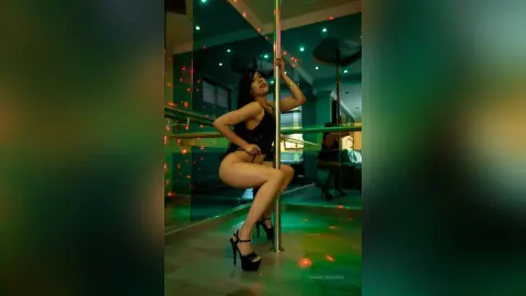 SamanthaHarvey poses naked against a silver pole, wearing black high-heeled sandals and looking back over her shoulder.