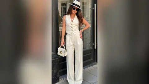 Stylish woman in a chic white vest and wide-leg trousers outfit posing outside a modern building.