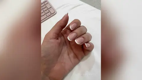 Close-up of a hand with elegant white French tip manicure resting on a white surface.