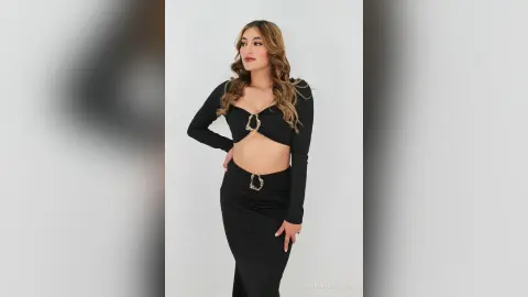 Stylish woman in a black long-sleeve crop top and matching maxi skirt posing against a white studio background.