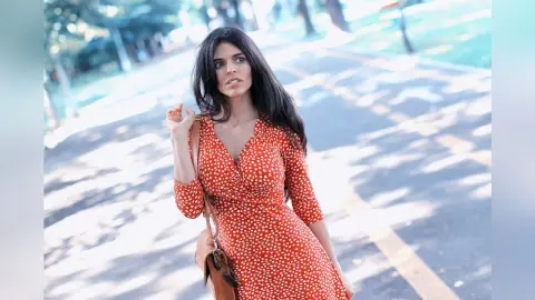 Young woman in a red floral summer dress walking along a sunny outdoor path.