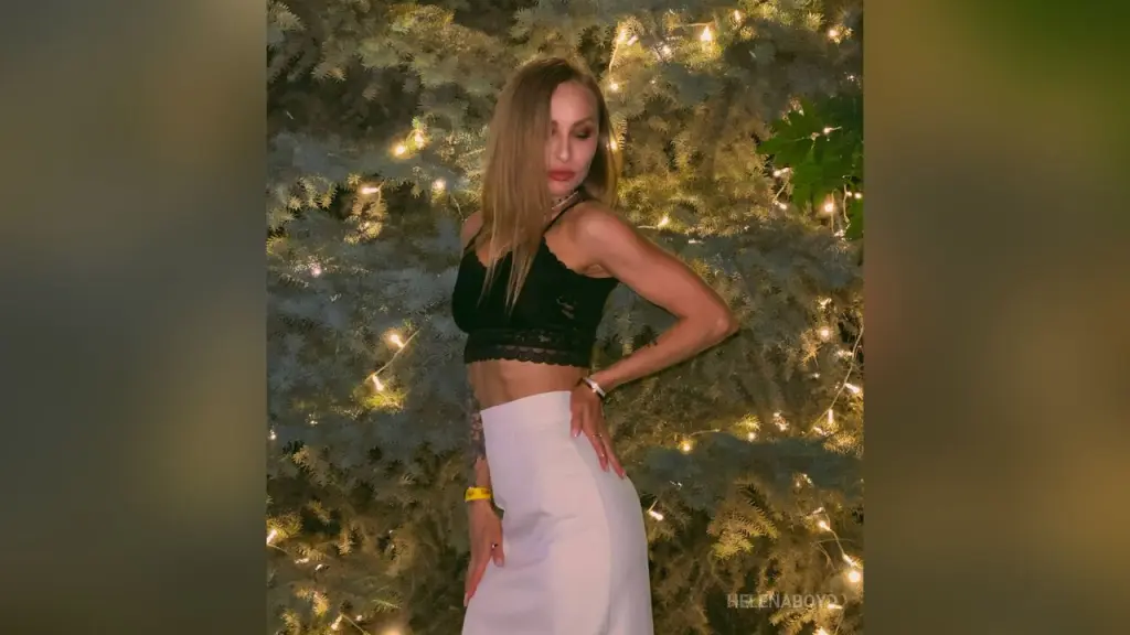 HelenaBoyd sits in a vintage chair wearing glasses, a black lace crop top, and white pants.
