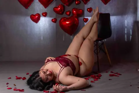 Curvy woman in red lace lingerie lying on floor amidst red heart decorations for a romantic Valentine's mood.