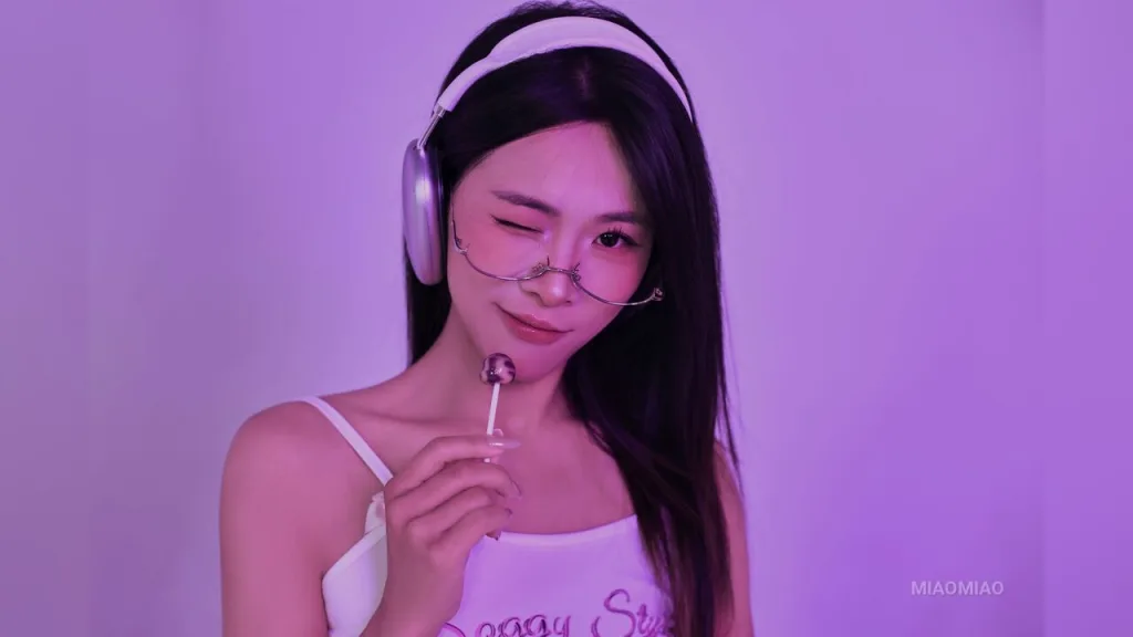 miaomiao — miaomiao winks while wearing white headphones and holding a lollipop against a purple background.