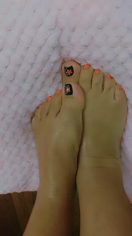 Close-up of feet with orange floral nail art resting on a soft pink textured rug.