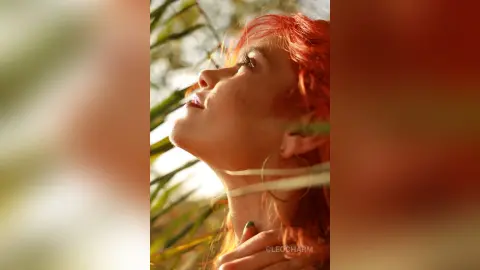 Dreamy side profile of a woman with red hair looking up in a sunlit garden setting.
