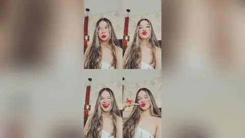 Young woman with long hair and red lipstick posing in a white top against a patterned wall background.