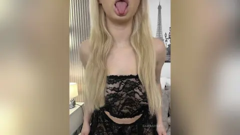 Blonde woman in a black lace crop top posing in a bright room with Eiffel Tower decor.