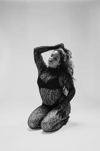 Elegant woman in a black lace bodysuit posing against a minimalist white background in a moody black and white style.