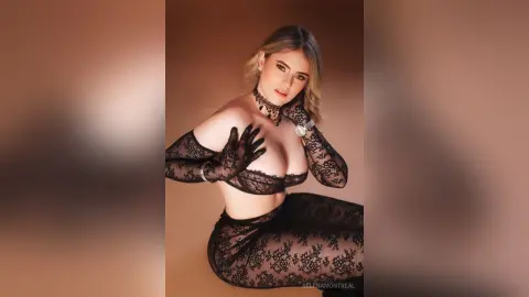 Elegant woman in black lace lingerie and sheer gloves posing against a warm brown background.