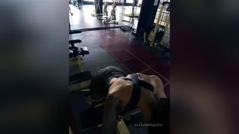 Tattooed woman in black athletic wear performing floor exercises in a modern gym setting.