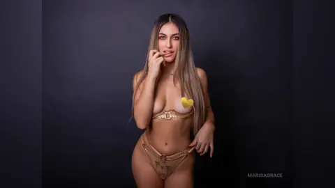 Young woman in a gold bikini posing confidently against a dark studio background.