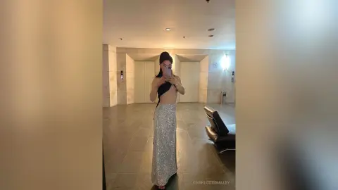 Woman in a black halter top and silver sequin maxi skirt taking a mirror selfie in a modern hotel lobby.