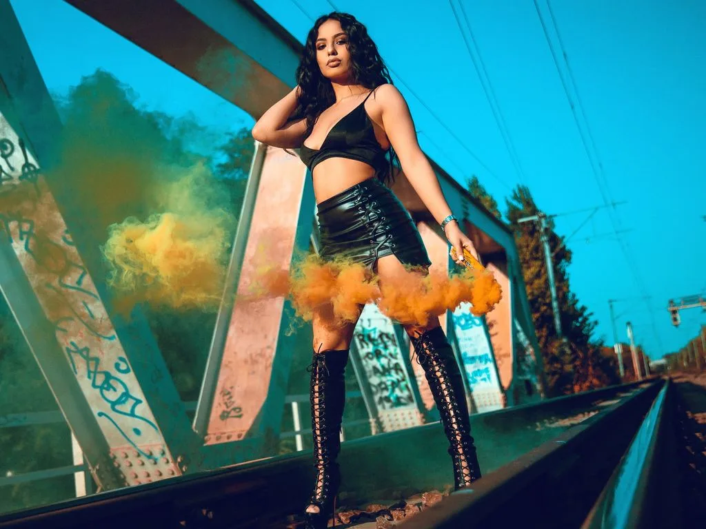 ErinAzzaro — ErinAzzaro stands on railroad tracks in a black crop top and leather miniskirt amidst clouds of yellow smoke.