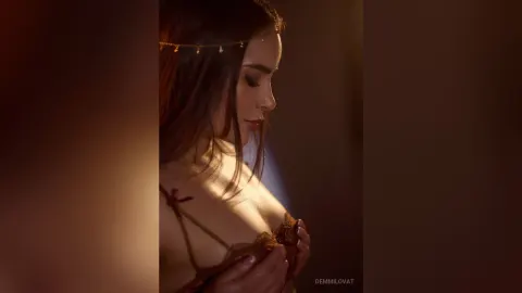 DemmiLovat — DemmiLovat poses in profile wearing a gold headpiece and brown lace lingerie while looking down.