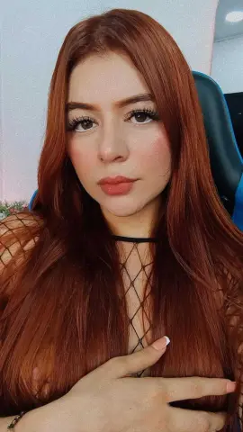 Redheaded woman in a black mesh top posing with a soft, natural look indoors.