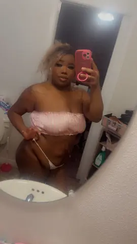 Curvy woman in a pink striped bikini top taking a mirror selfie in a bathroom.