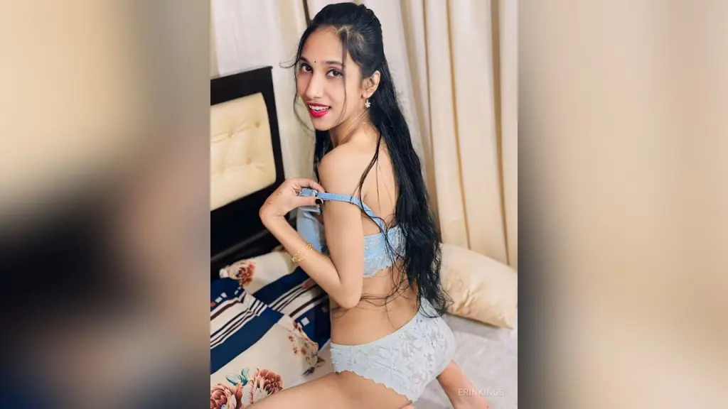 Young woman in white lace camisole relaxing on a bed in a cozy bedroom setting.