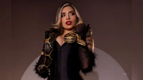 Glamorous woman in a black corset holding a large snake against a minimalist studio background.